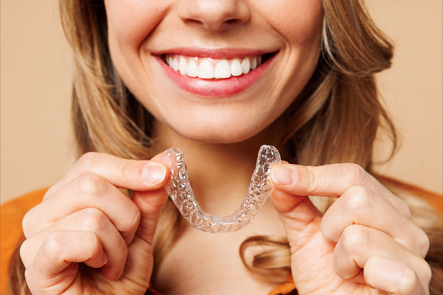 A close-up of a smiling woman holding a clear aligner