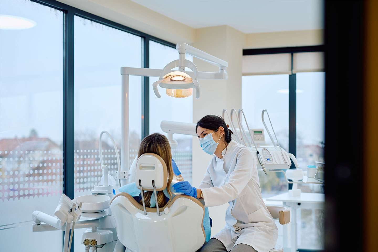 A masked dentist treating a patient inside a dental clinic.