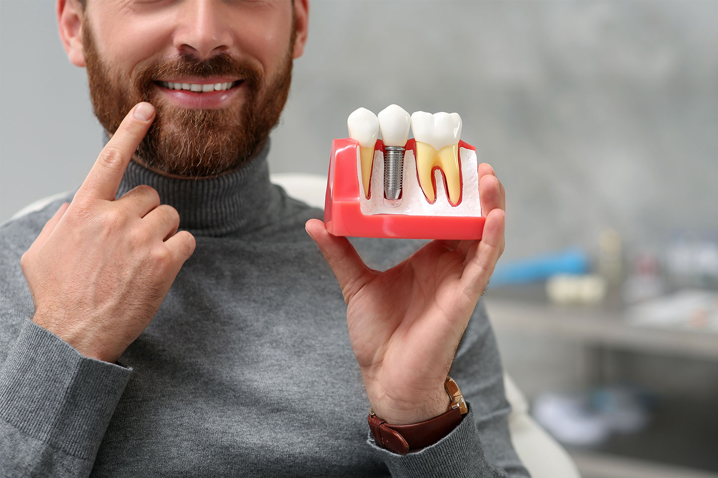 A man pointing at his teeth while holding a 3D dental implant model